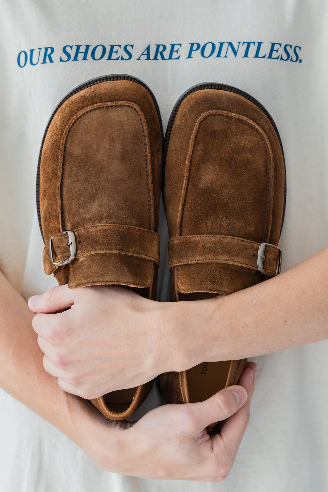 Man holding two wide toe box loafers with a shirt that says Our shoes are pointless